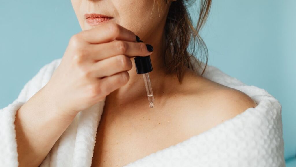 Aynada göz çevresindeki ince çizgilere serum uygulayan kadın