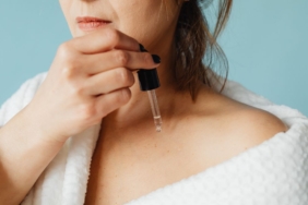 Aynada göz çevresindeki ince çizgilere serum uygulayan kadın